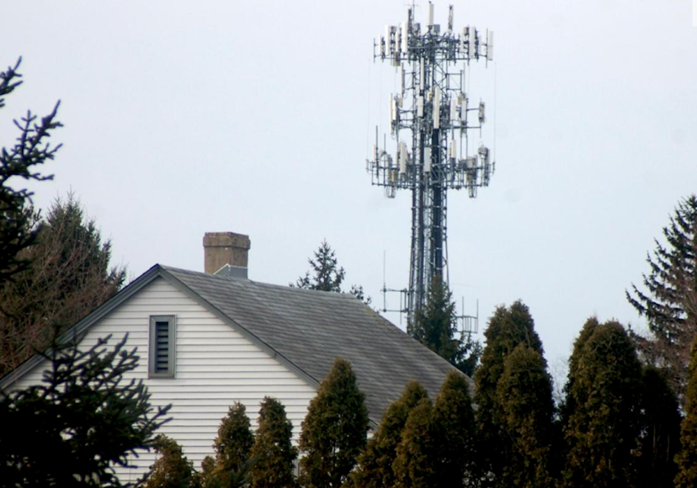 The Dangers of Cell Towers to Our Health 8 Cell tower with multiple wireless antennas rising above a residential home and surrounding trees.