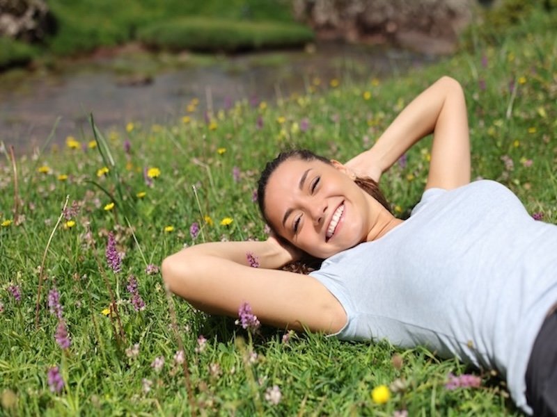 Earth Healing Frequency: Boost Health & Well-Being 5 Woman relaxing on her back in a grassy meadow with wildflowers, illustrating outdoor grounding, earthing, and wellness.
