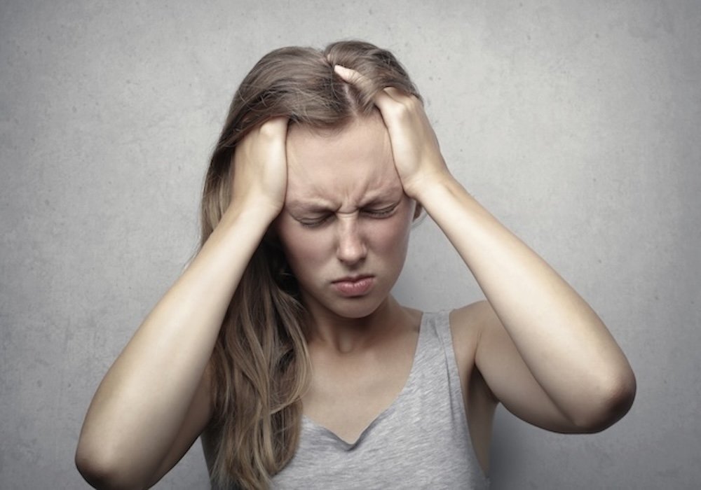 What is Electromagnetic Hypersensitivity? 4 Woman holding her head with both hands and appearing uncomfortable, illustrating an article about electromagnetic hypersensitivity and reported symptoms.